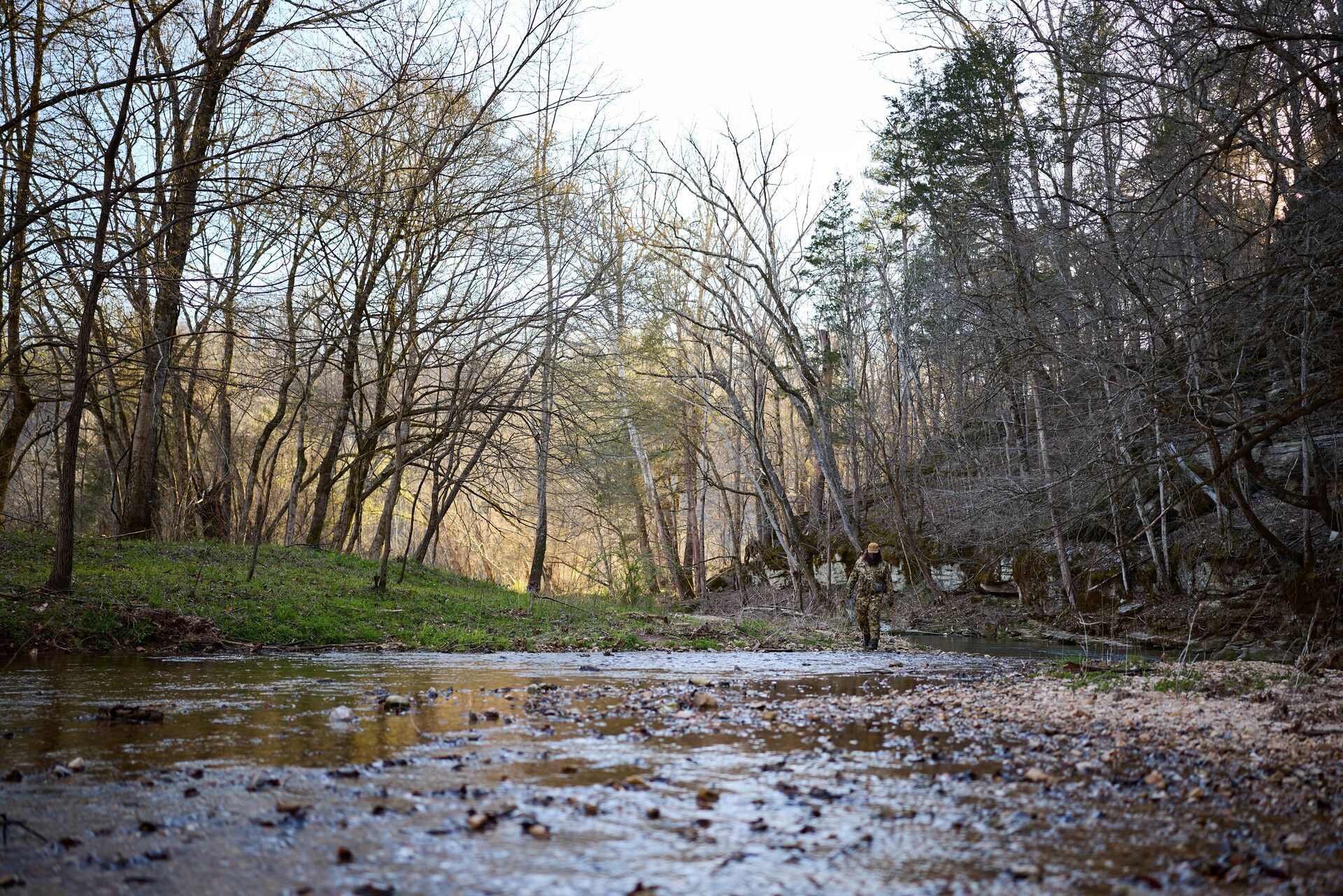 Water running through the woods, hunter down stream. 