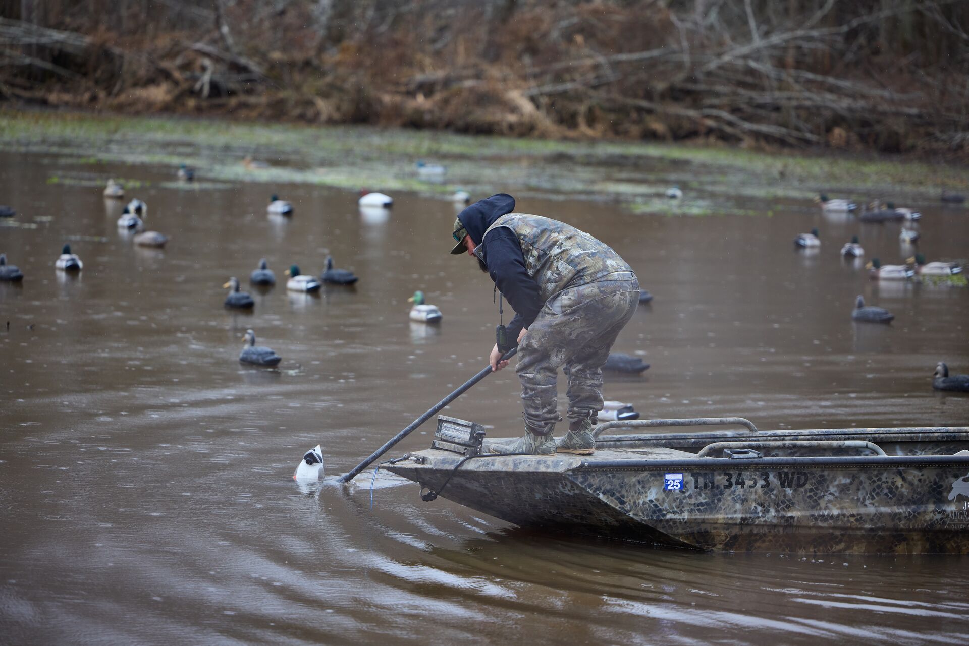 A waterfowl hunter in a boat places duck decoys. 