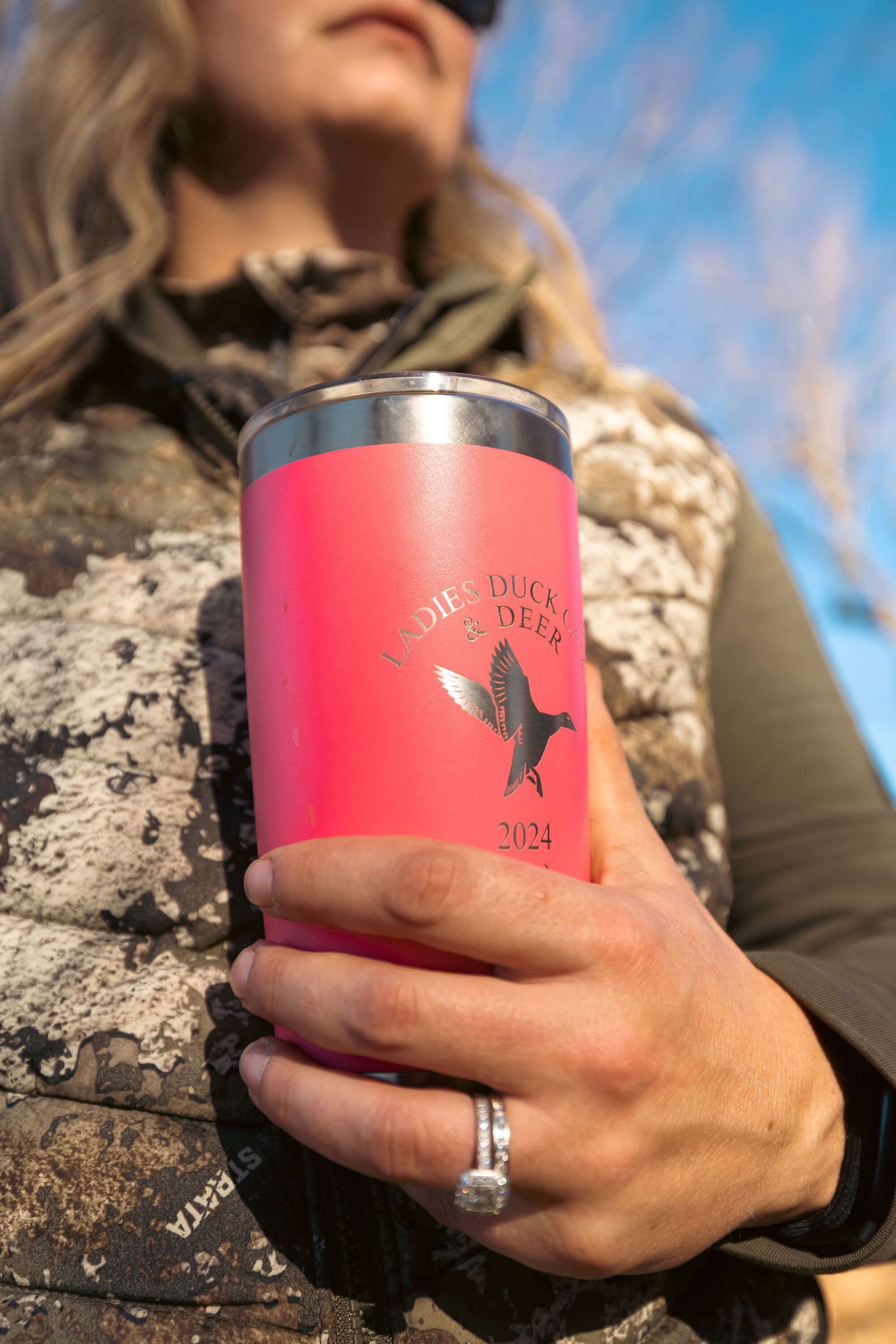 A woman hunter holds a tumbler while wearing camo for hunt. 