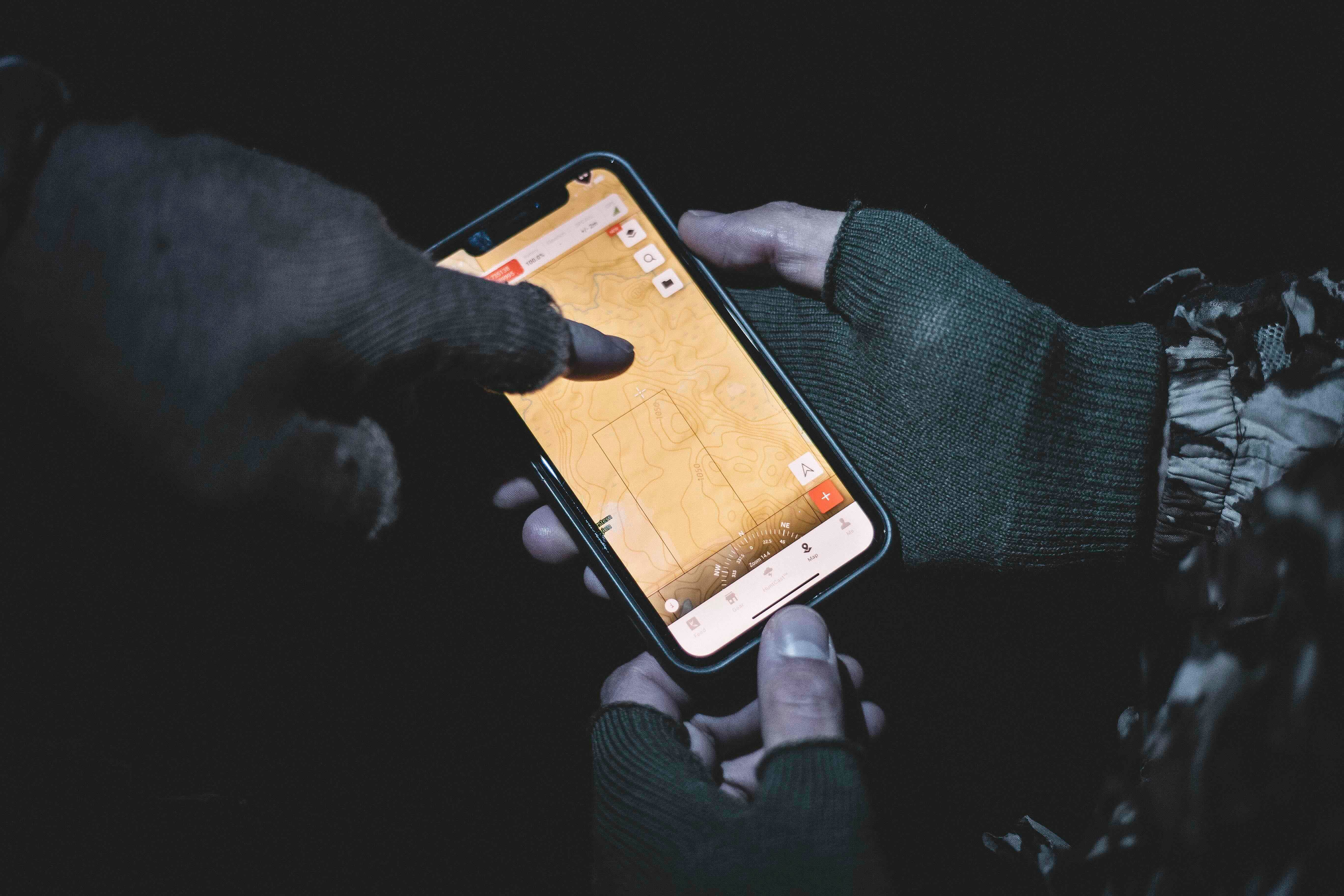 Close-up of hands pointing to HuntWise on a phone screen, marking deer feeder locations concept. 