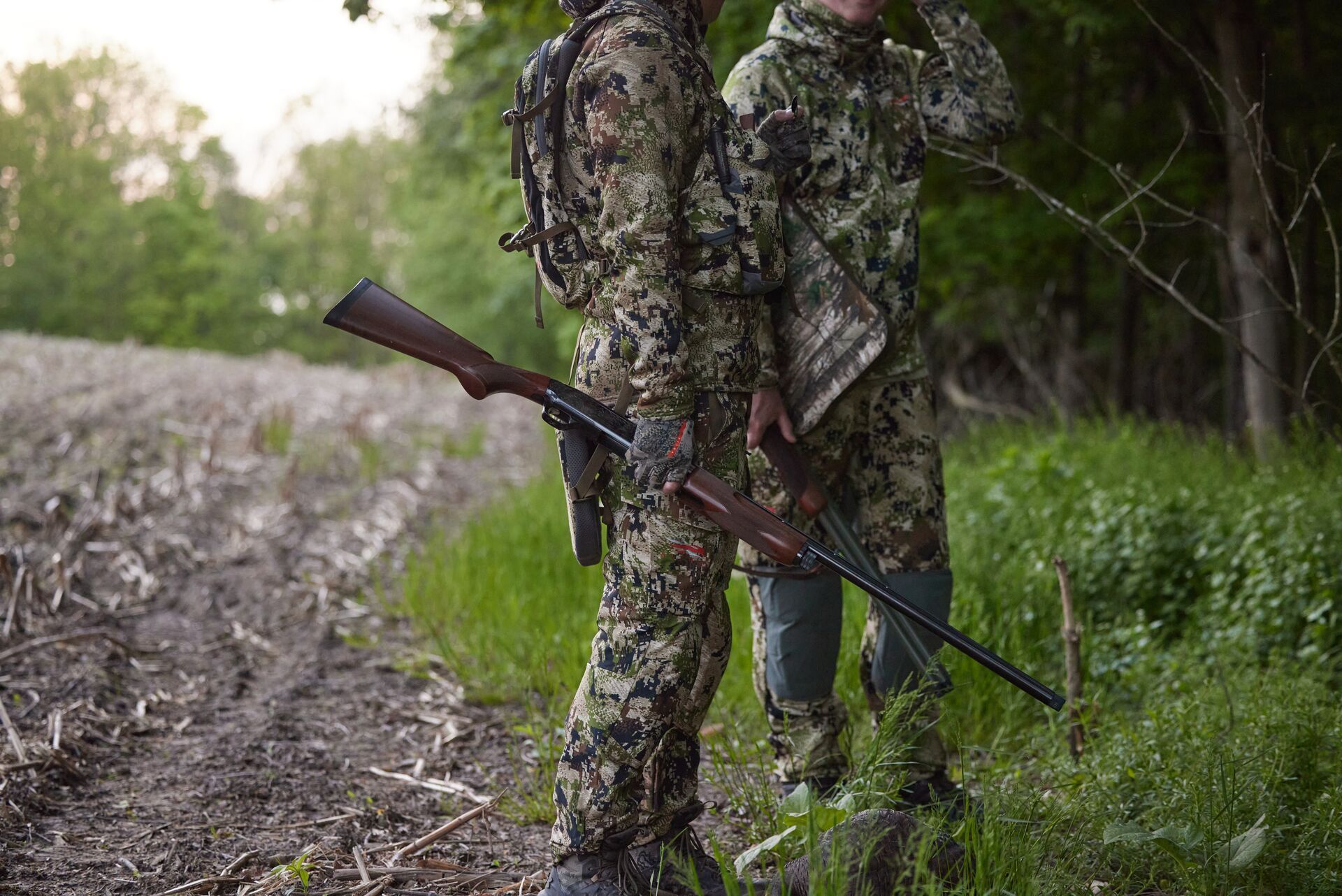 Two hunters in camo and holding firearms, represents the Gould's Turkey hunting experience. 