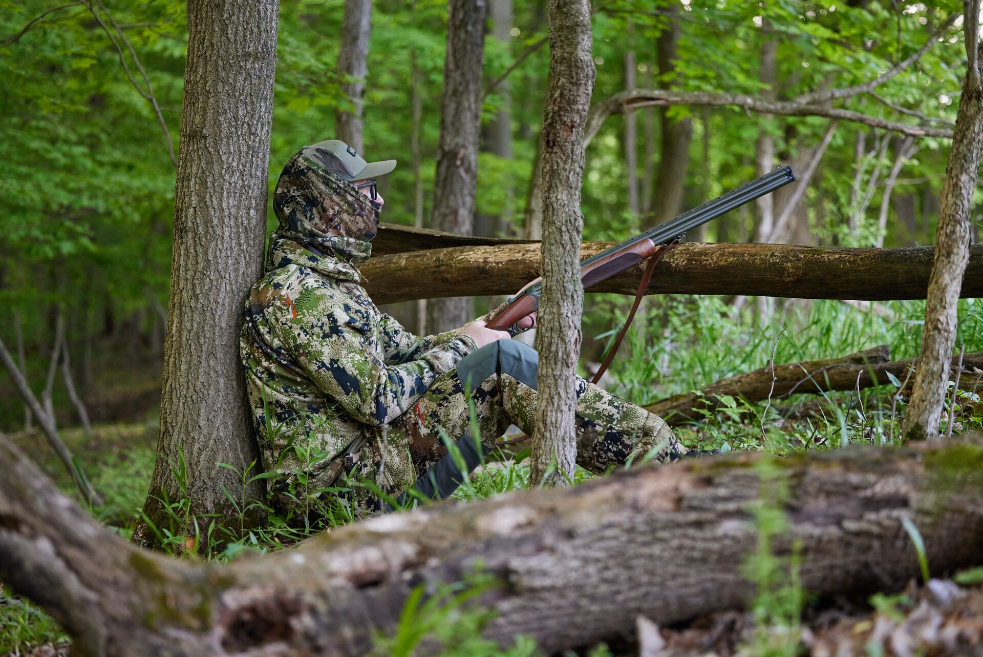 A hunter in camo sits against a tree with a firearm, hunting license in Mississippi concept. 