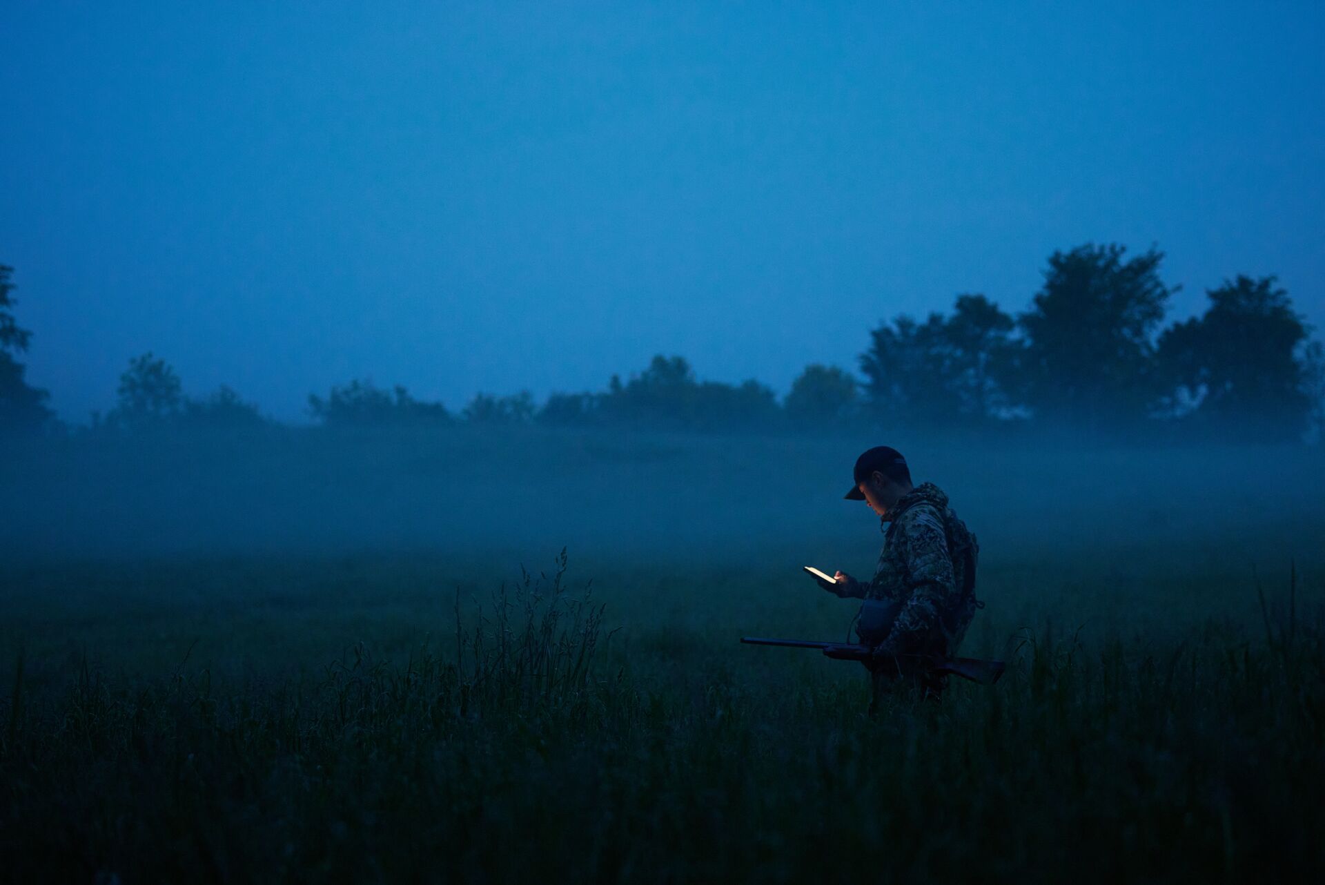 A hunter at dawn in a field looking at a cellphone, use HuntWise for a successful SC deer season concept. 