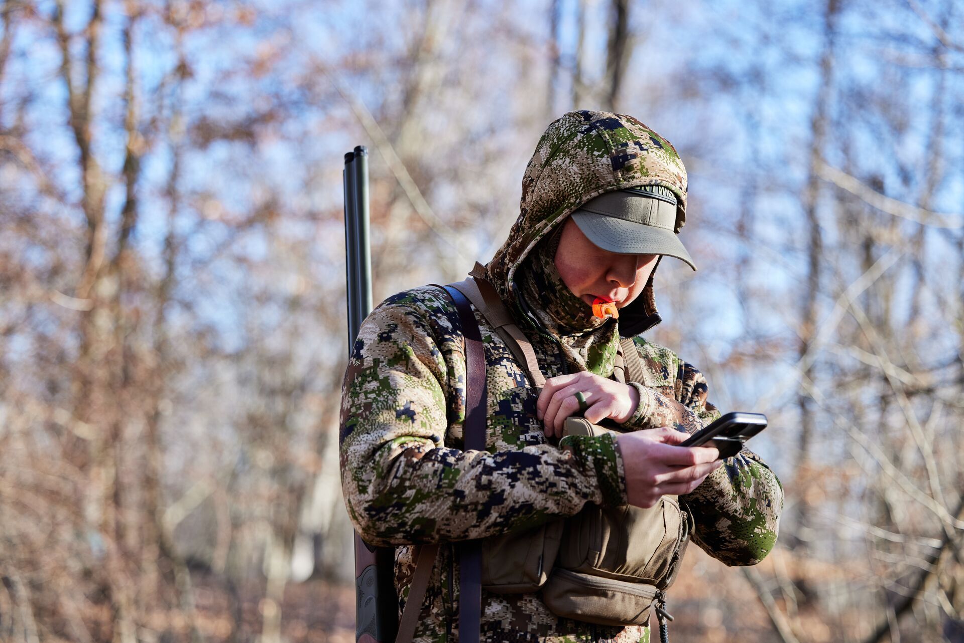 A hunter in turkey camo with a turkey call looks at a phone, use the HuntWise app to hunt turkey. 