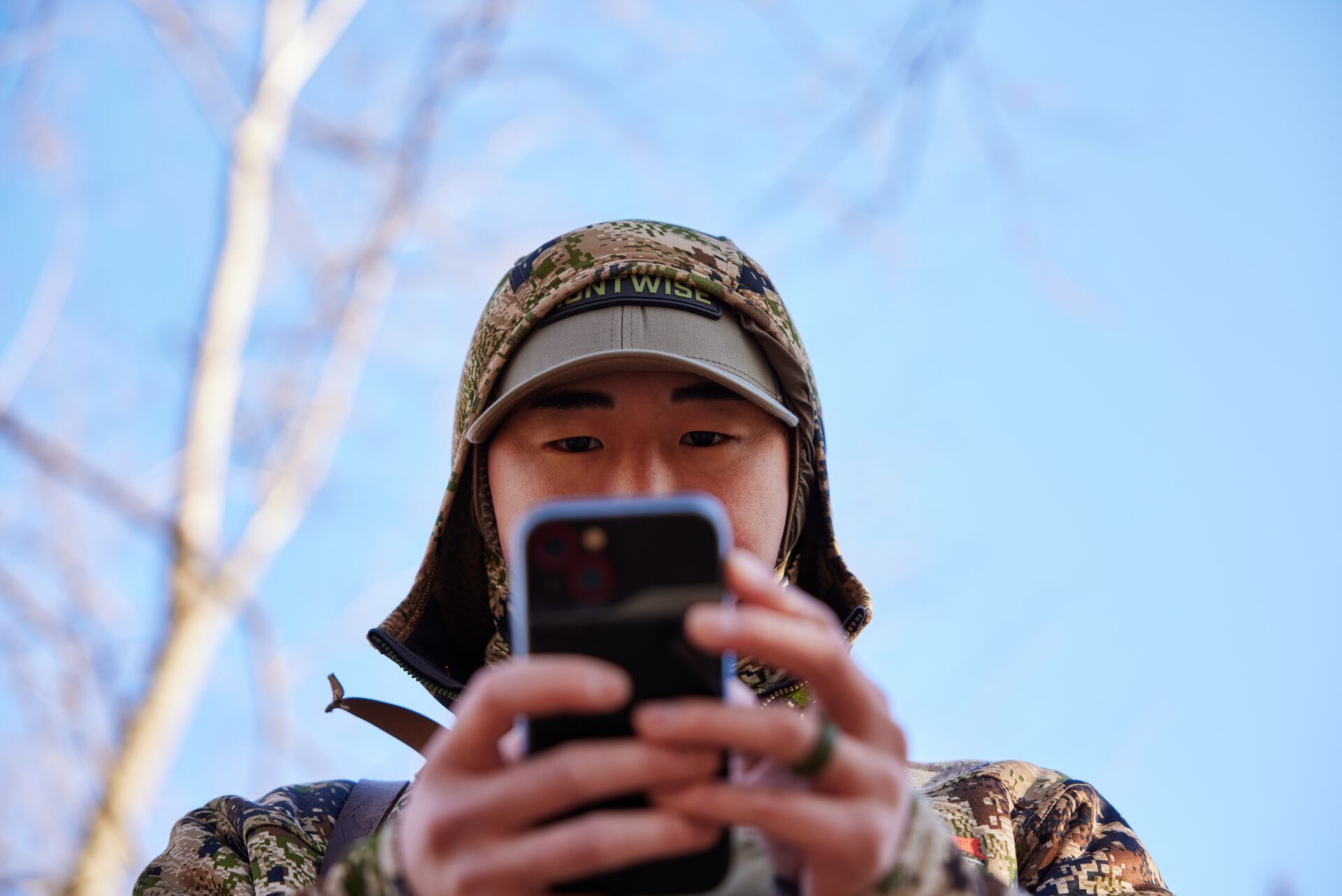 A hunter in camo looks at a phone in his hands, using a hunting app concept. 