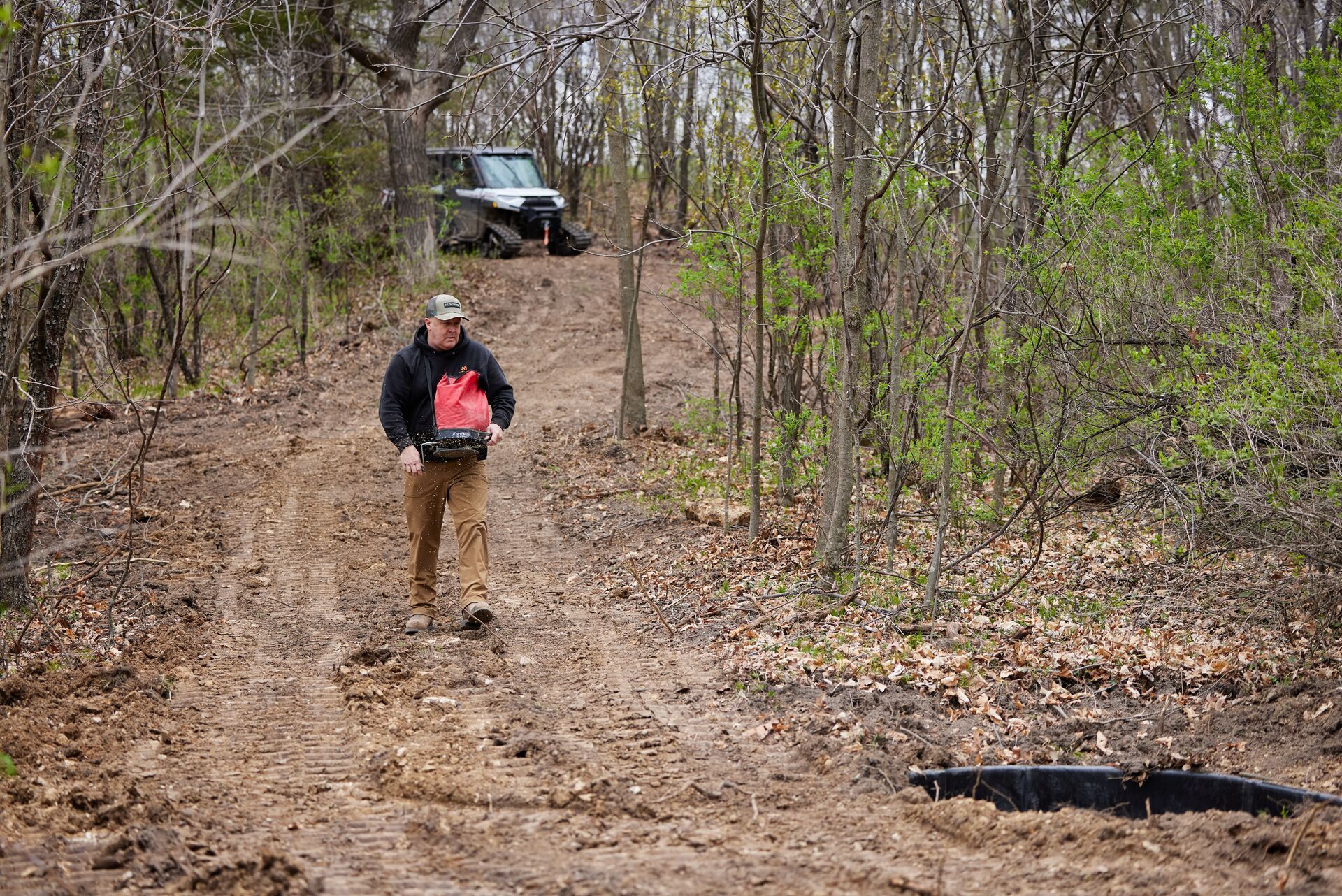 Jeff Sturgis walks a dirt path carrying a seed bucket for a food plot, moon phases and deer movement concept.