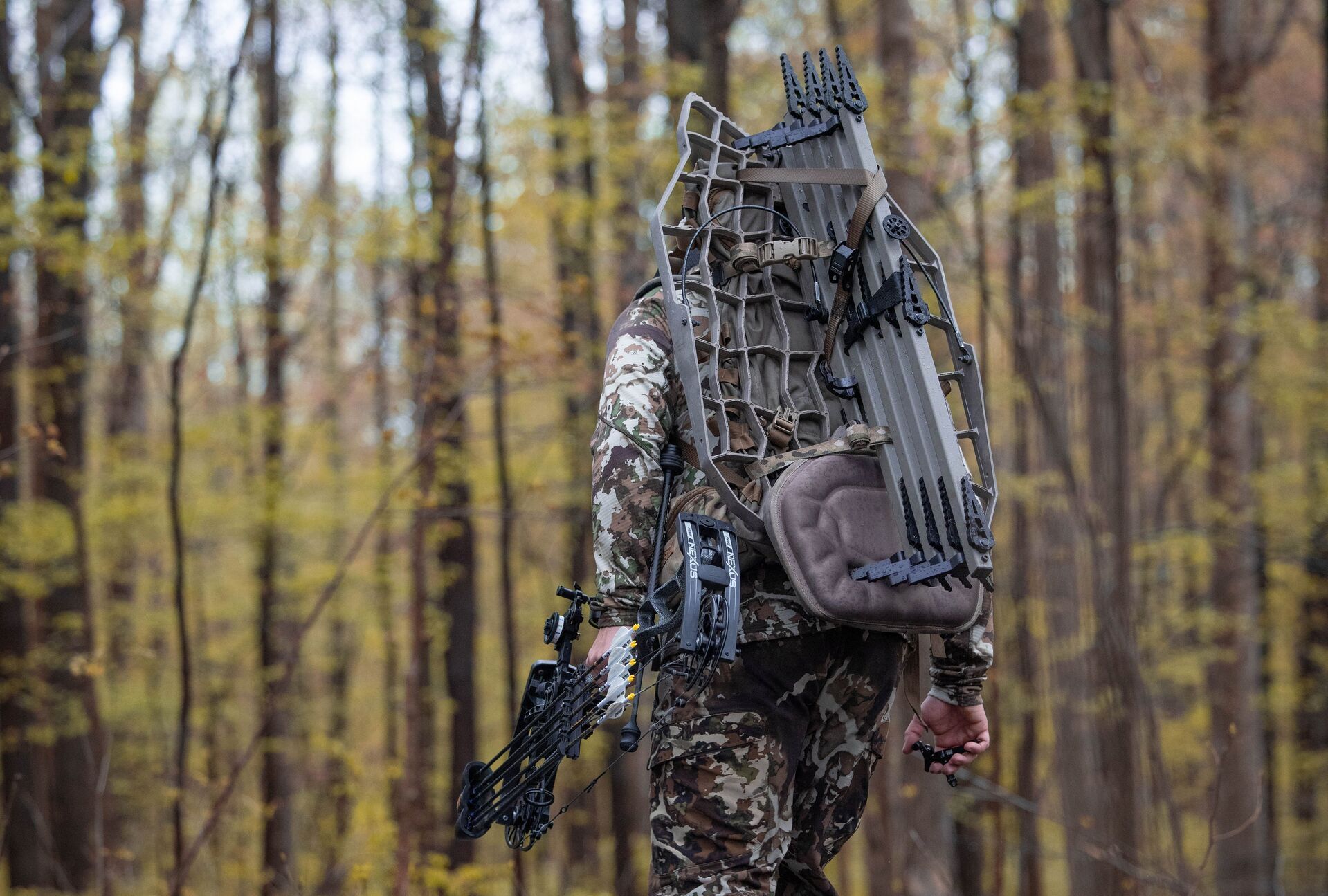 A hunter wears camo and carries a tree stand and bow, hunting Alabama deer season concept. 