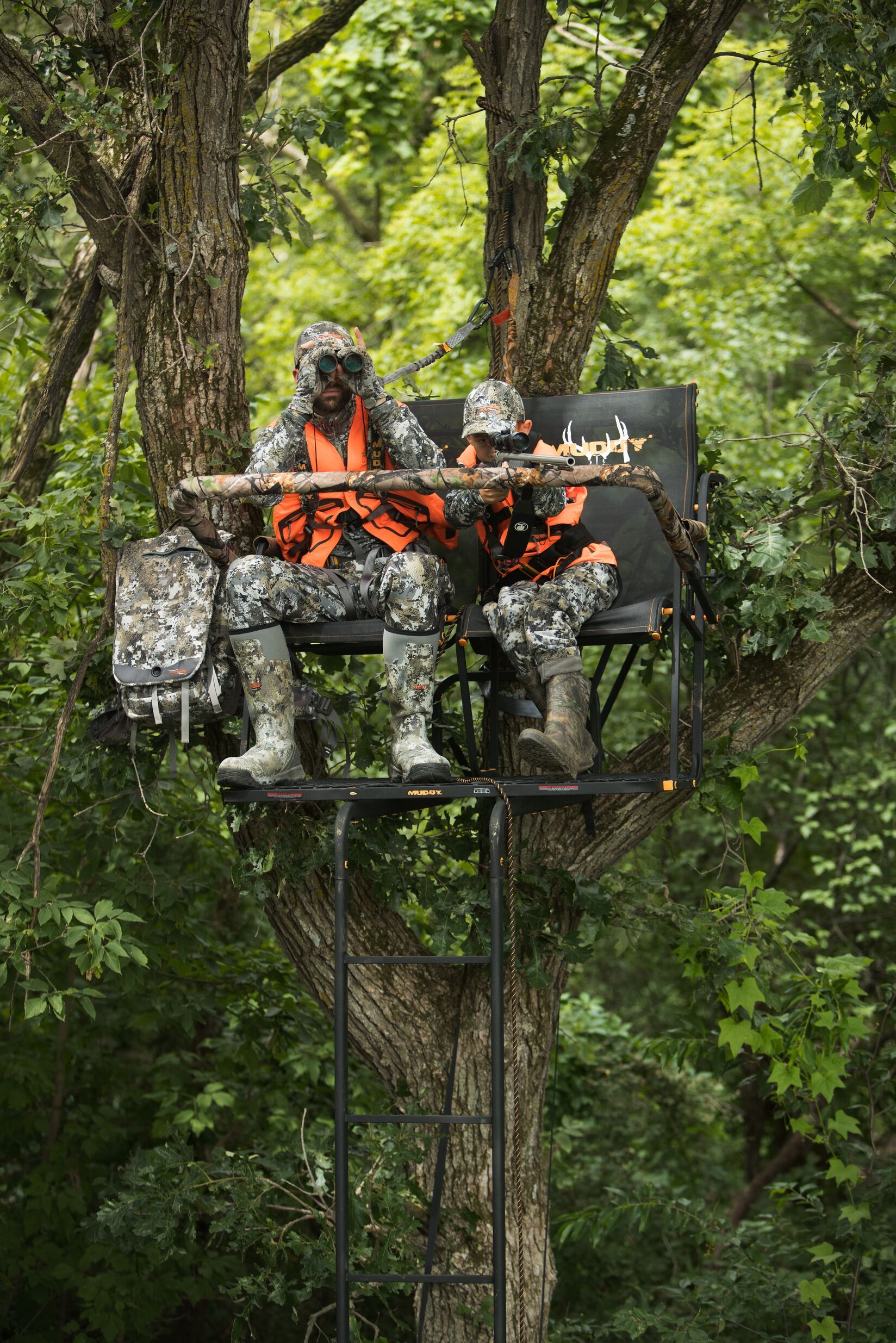 A man and boy in camo in a tree stand using binoculars and a rifle, deer season Florida concept. 