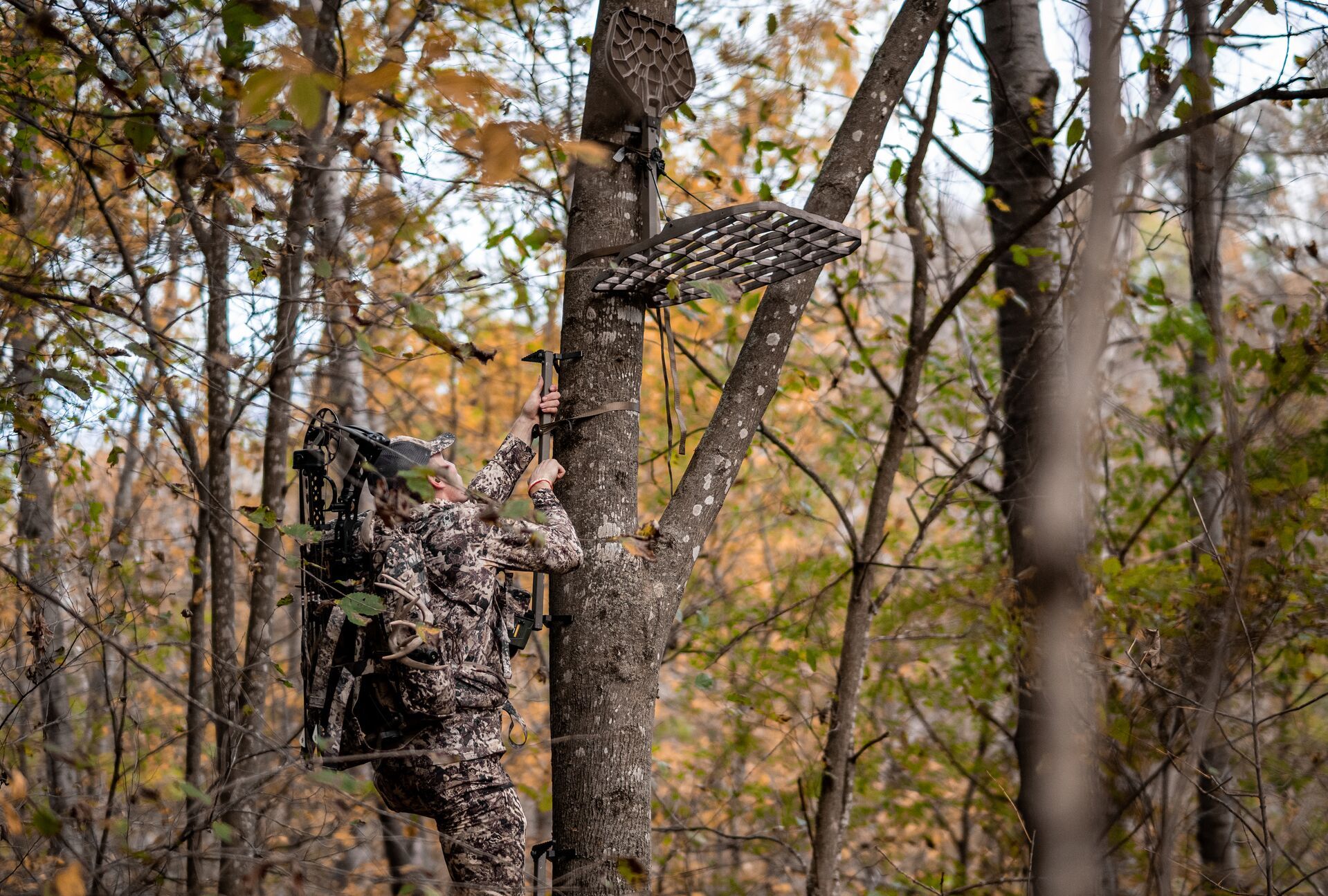 A hunter in camo climbs into a tree stand, deer hunting season in New York concept. 