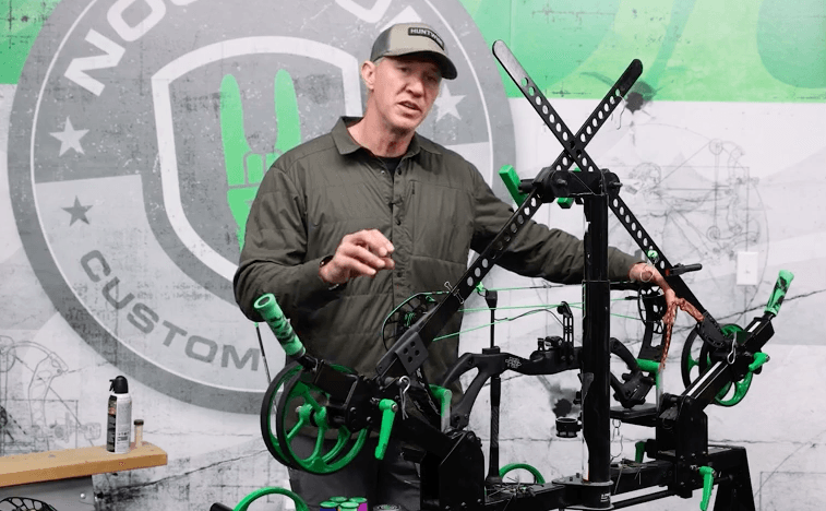 John Dudley stands behind a compound bow on a rack to talk about maintenance. 