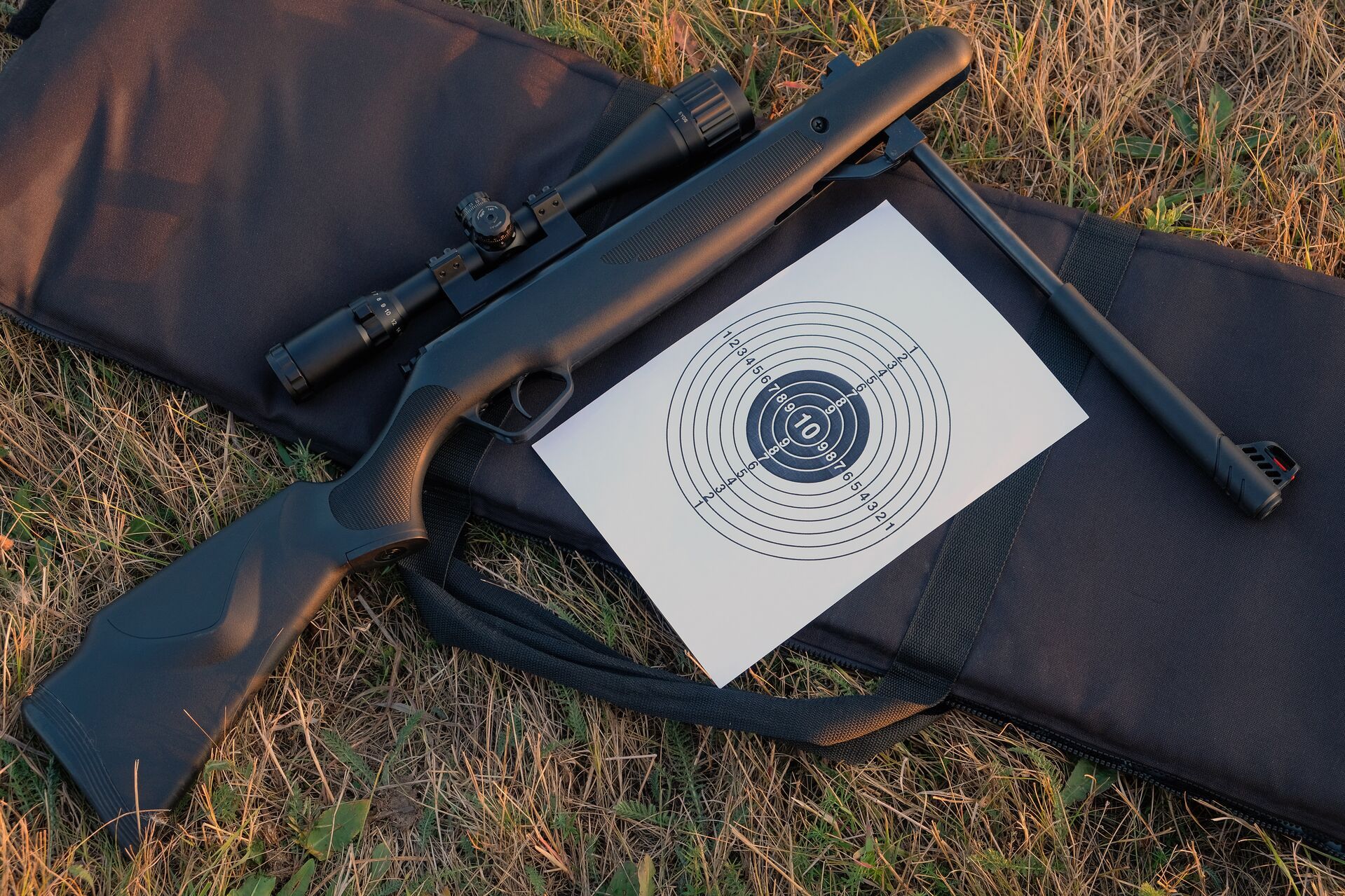 An air rifle laying on a gun case next to a target. 